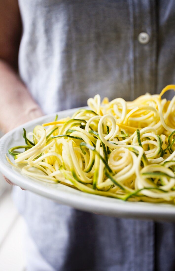 A person holding a plate of raw sprial-cut courgette