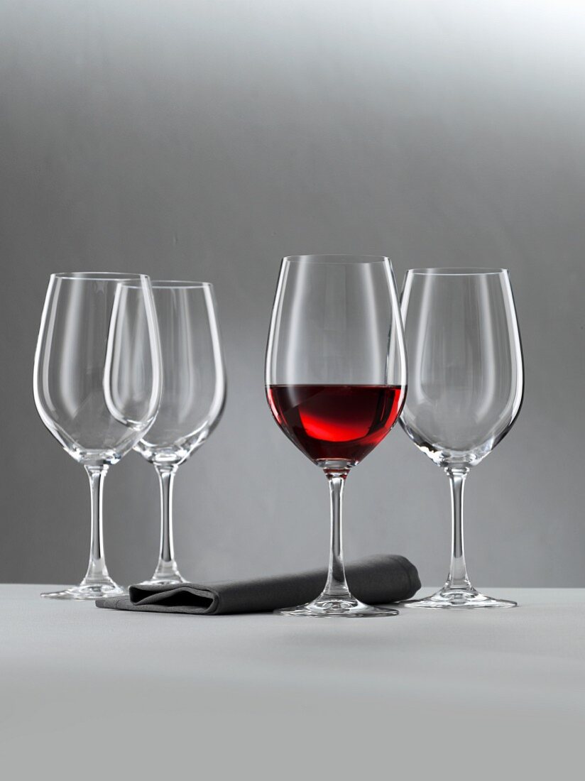 A glass of red wine and three empty wine glasses against a grey background