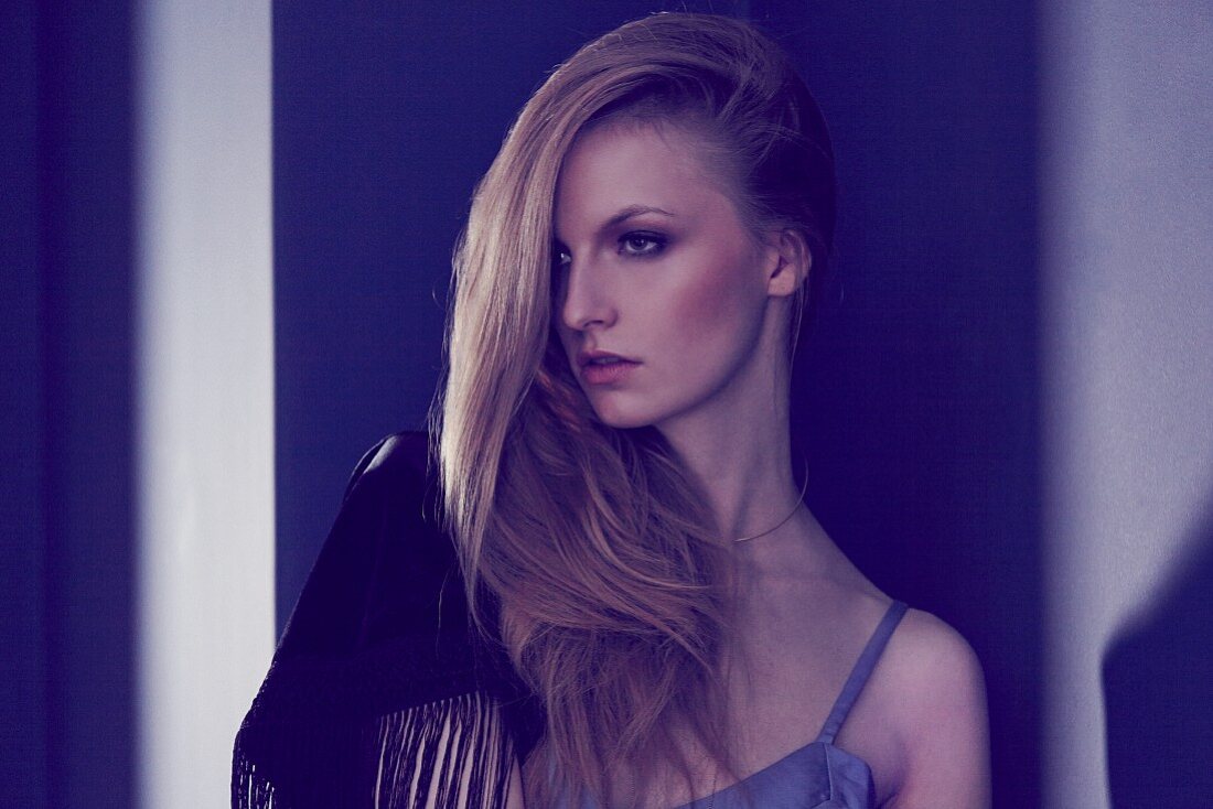 Portrait of a blonde woman wearing a vest top and a fringed shawl over her shoulder