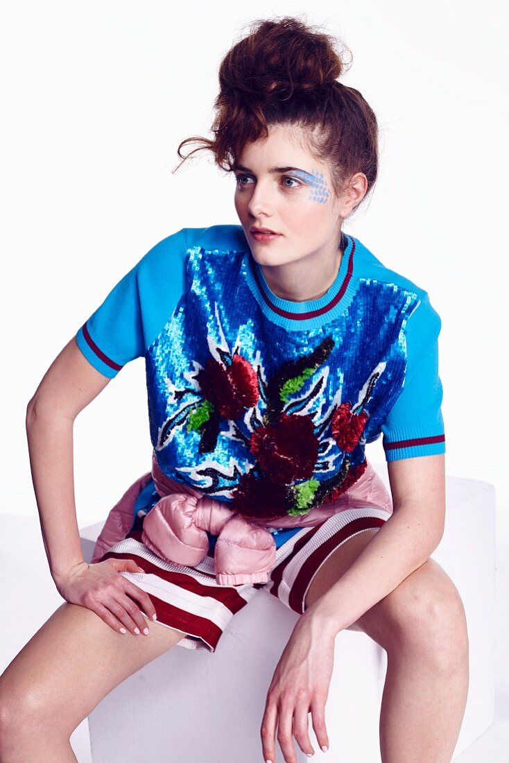 A young woman wearing a colourful outfit sitting on a stool