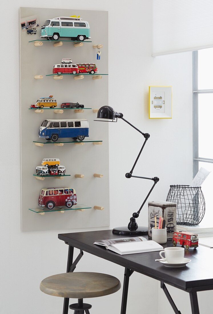 Shelves for toy cars on a wall with a desk and a retro lamp in front of them