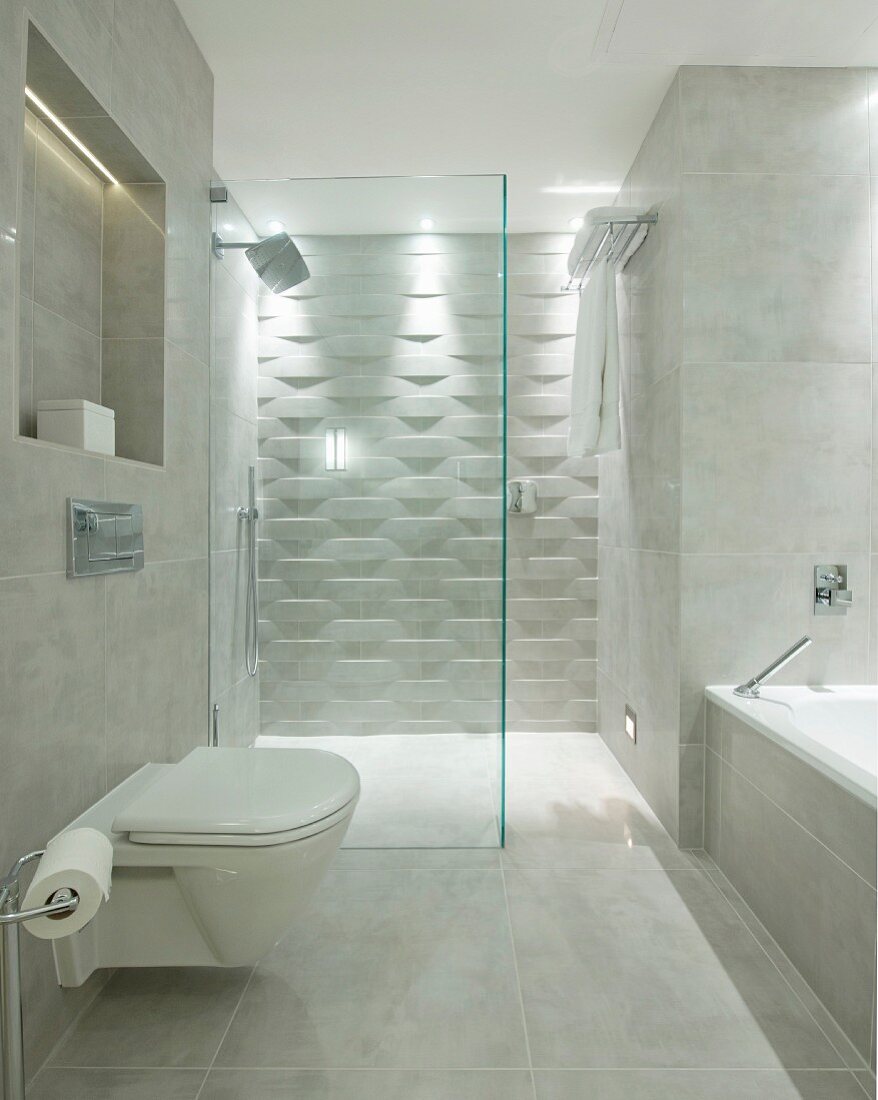 WC und Badwanne in Designerbad mit Marmorfliesen, im Hintergrund begehbare Dusche mit Fliesen in 3D