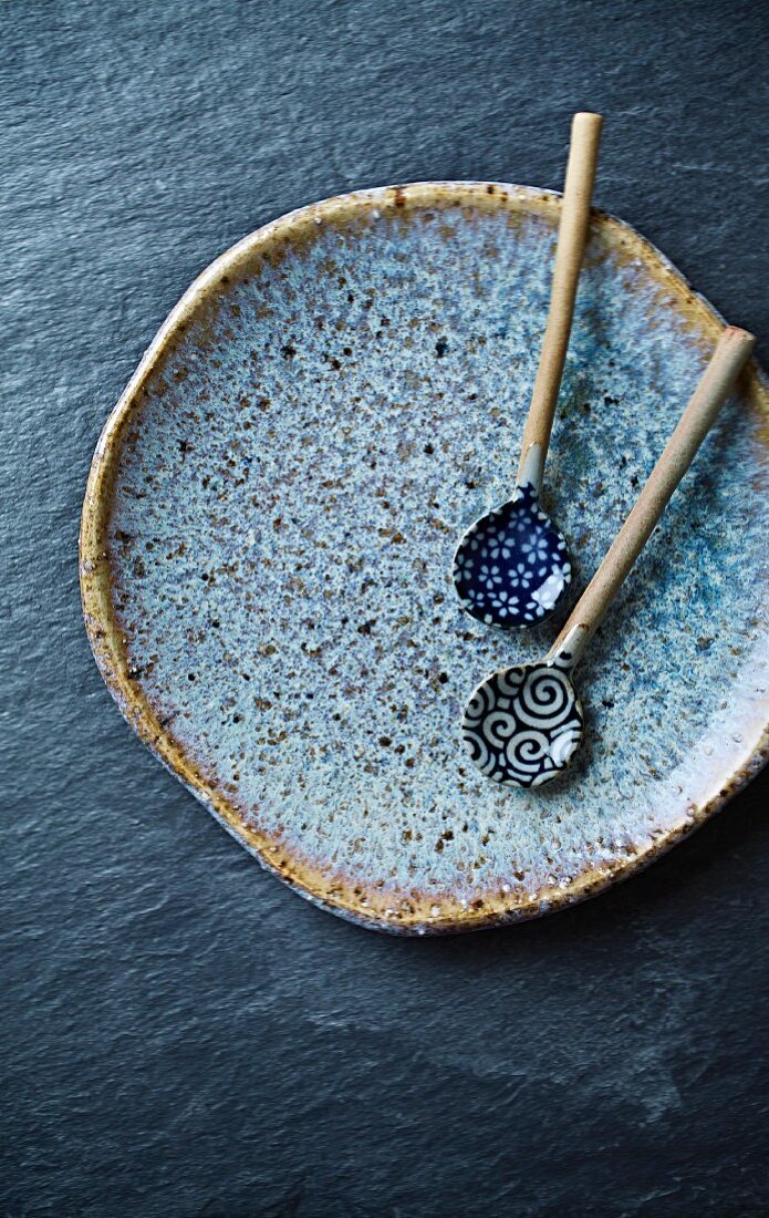 Zwei handgefertigte Keramiklöffel auf blauem Keramikteller (Asien)