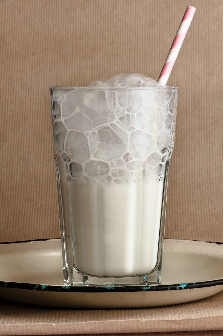 A glass of foamy milk with a straw