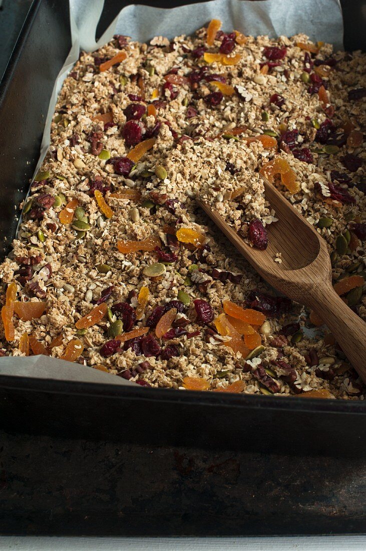 Homemade muesli in a baking tray with a wooden scoop