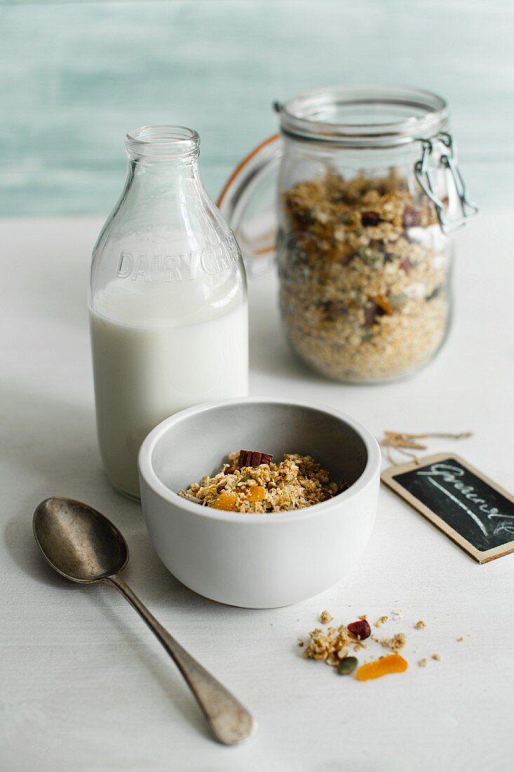 A bowl of muesli with a bottle of milk and a jar of muesli in the background