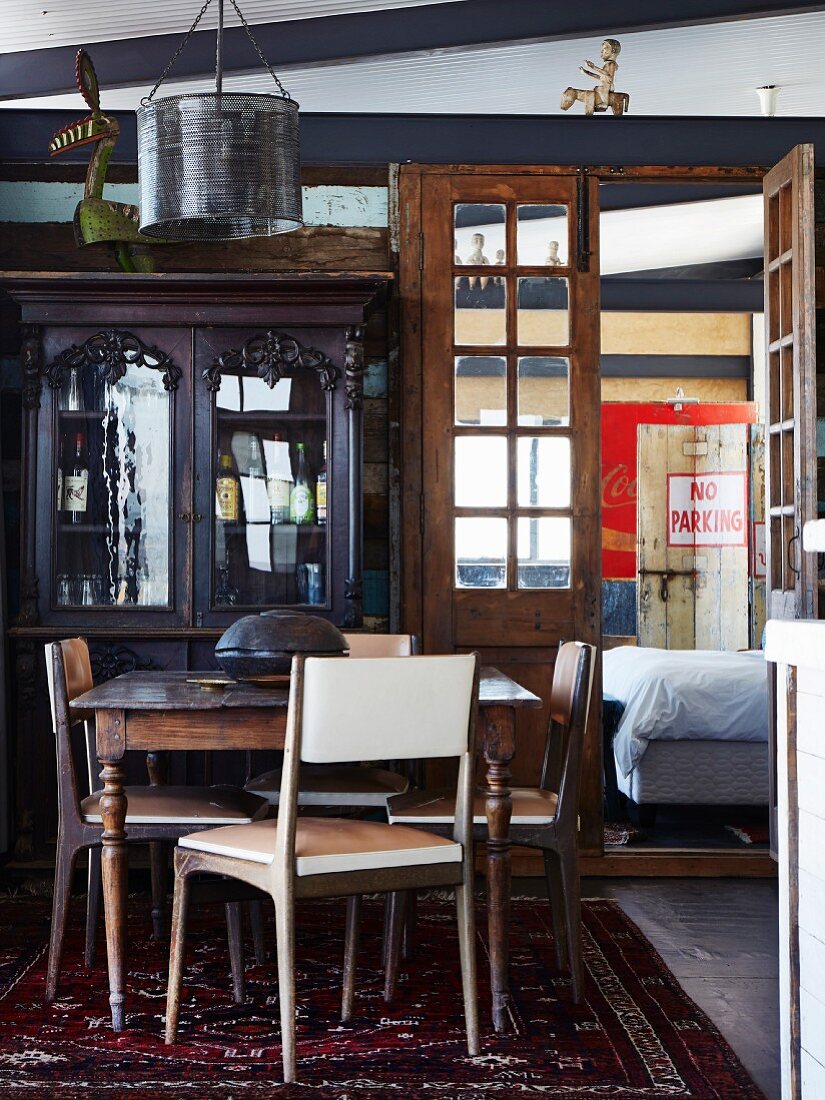 Retro chairs around wooden table in front of antique cabinet with glass-fronted top section next to open double doors