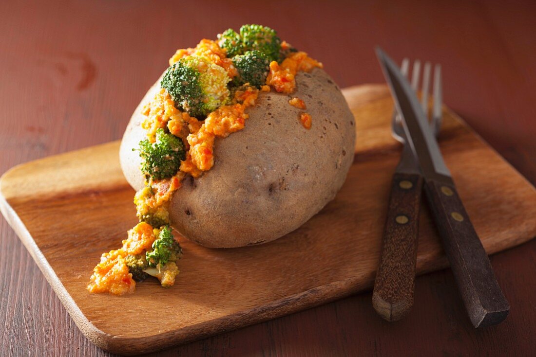 A baked potato with broccoli and vegan cheese sauce on a chopping board