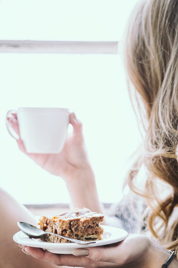 A woman holding a slice of apple and walnut cake and a cup of coffee