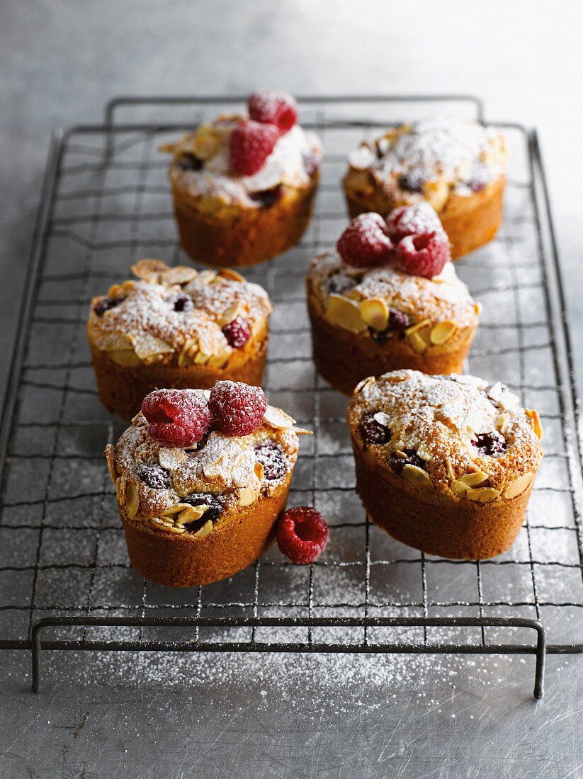 Friands with raspberries, lemons and flaked almonds on a wire rack