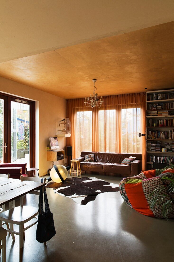 Patchwork beanbag and animal-skin rug in front of brown leather couch in cosy living area