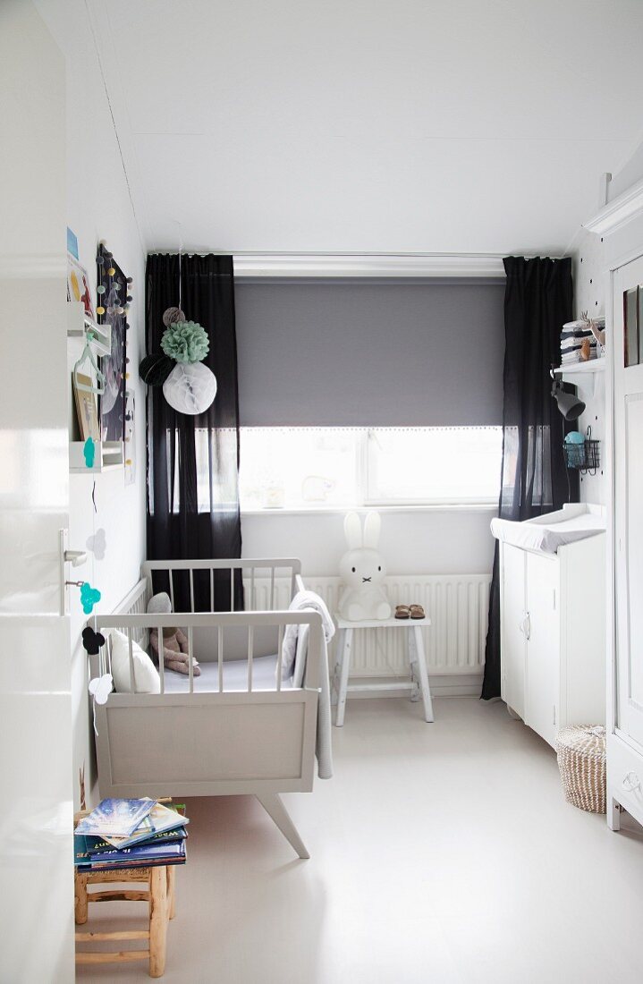 Retro cot, changing cabinet, grey roller blind and black curtains in nursery