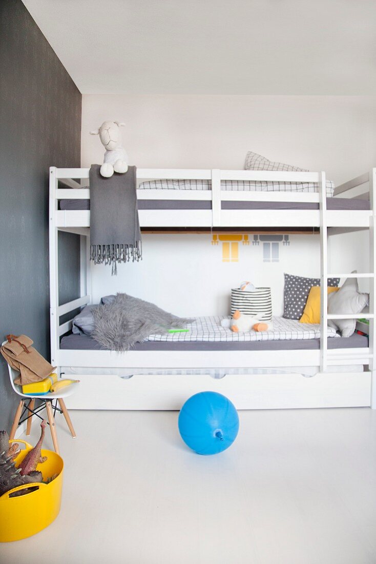 Reduziertes Jungenzimmer mit weißem Stockbett und grauer Tapete, dazu gelbe und blauer Farbakzent