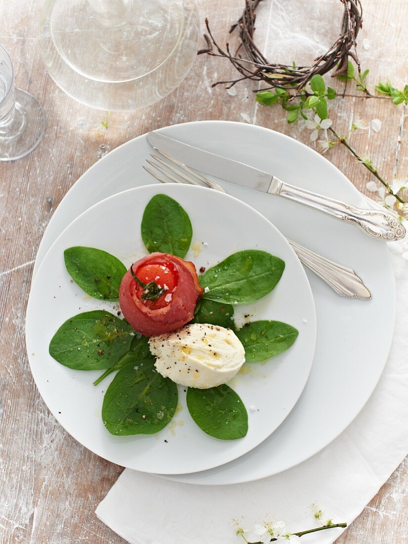 An oven-roasted tomato wrapped in ham with mozzarella on spinach leaves