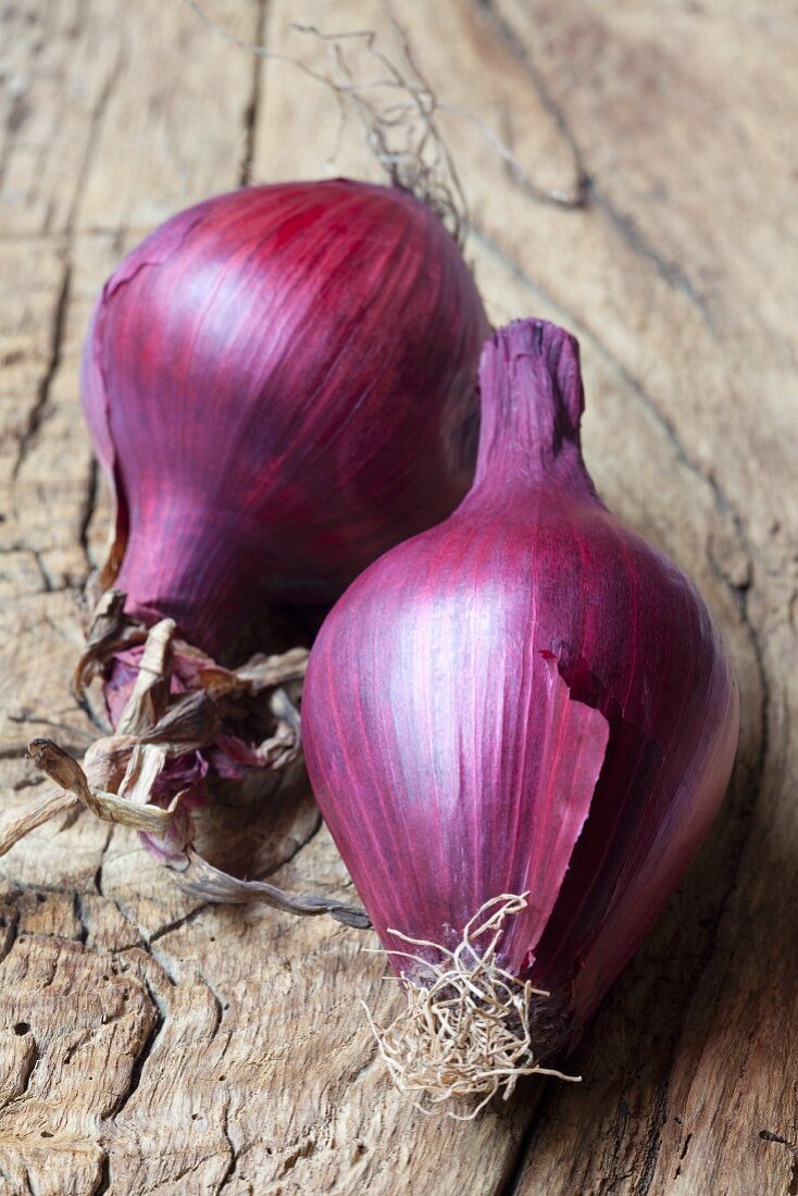 Two red onions on a wooden surface