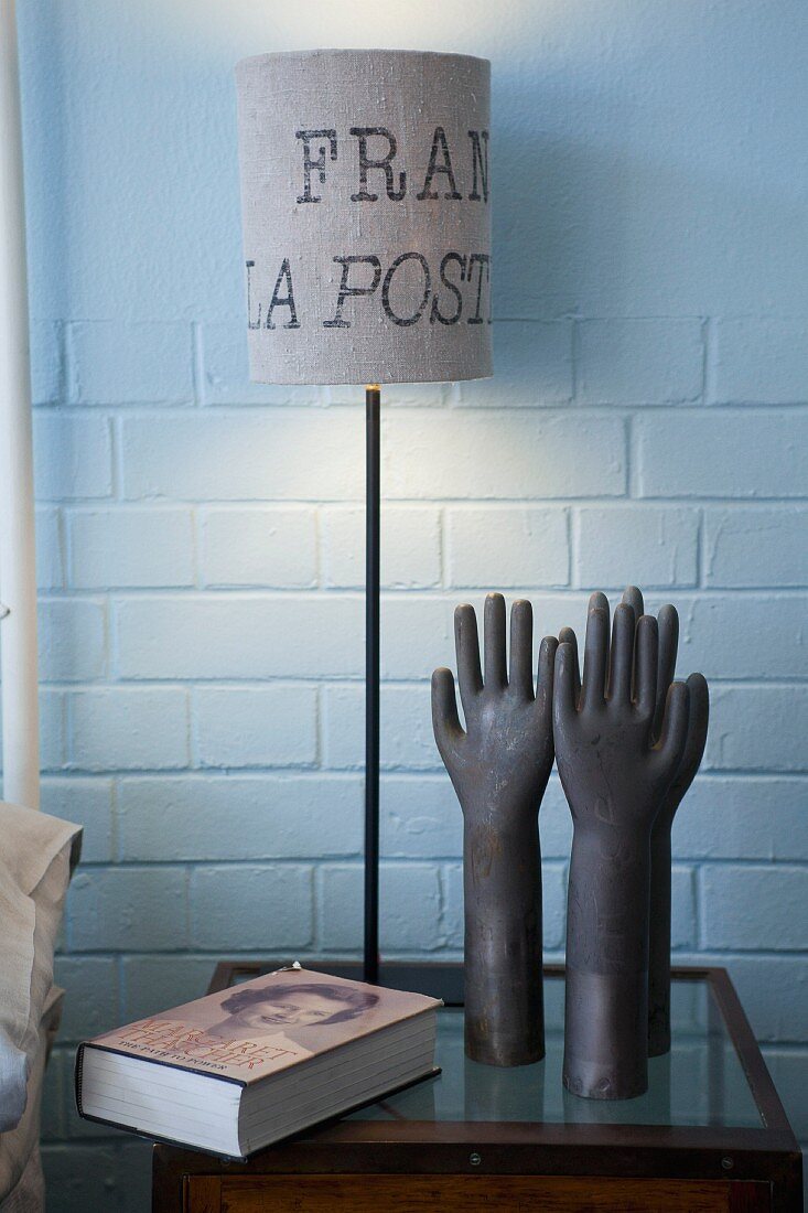 Table lamp with lettering on lampshade and hand-shaped ornaments on small bedside table