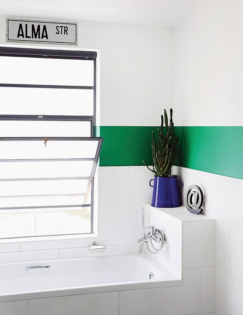 Badewanne vor Fenster mit Kippfenster in weißem Bad mit grünem Streifen