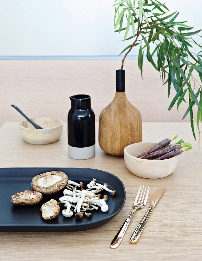 Various mushrooms on black dish, bowls and branch of leaves in wooden vase