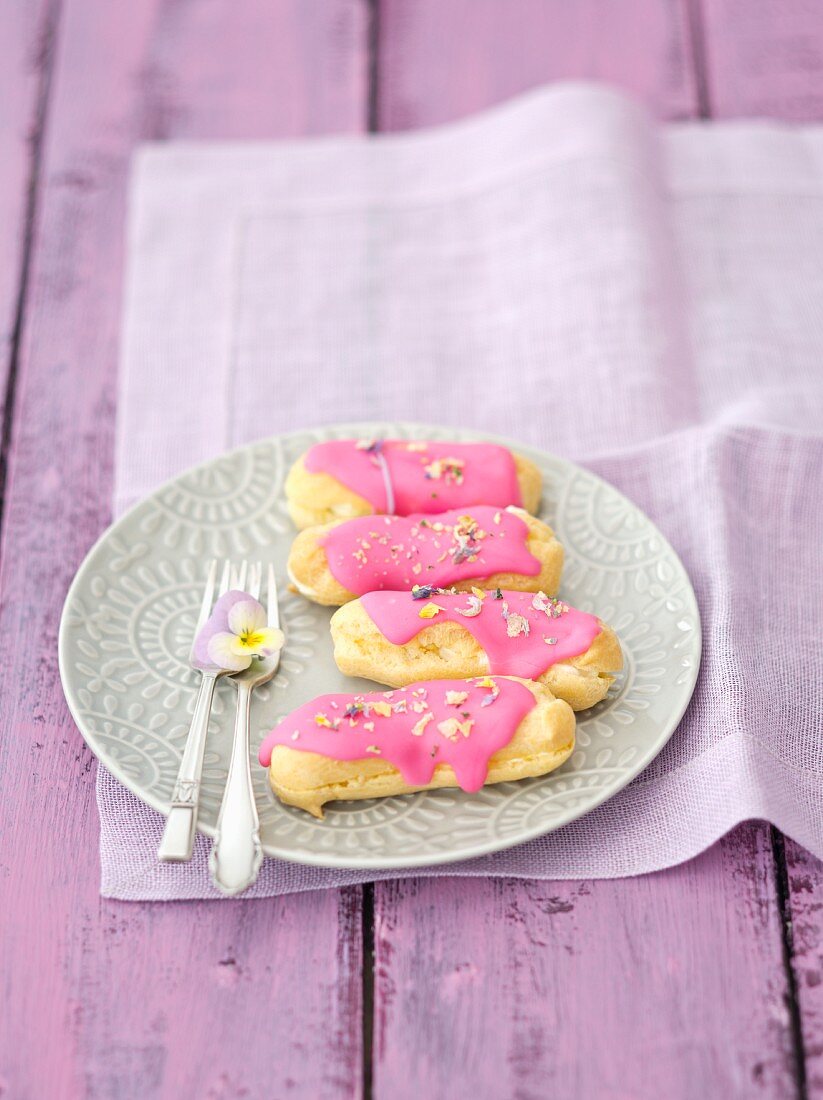 Eclairs mit rosa Zuckerguss und getrockneten Stiefmütterchenblüten