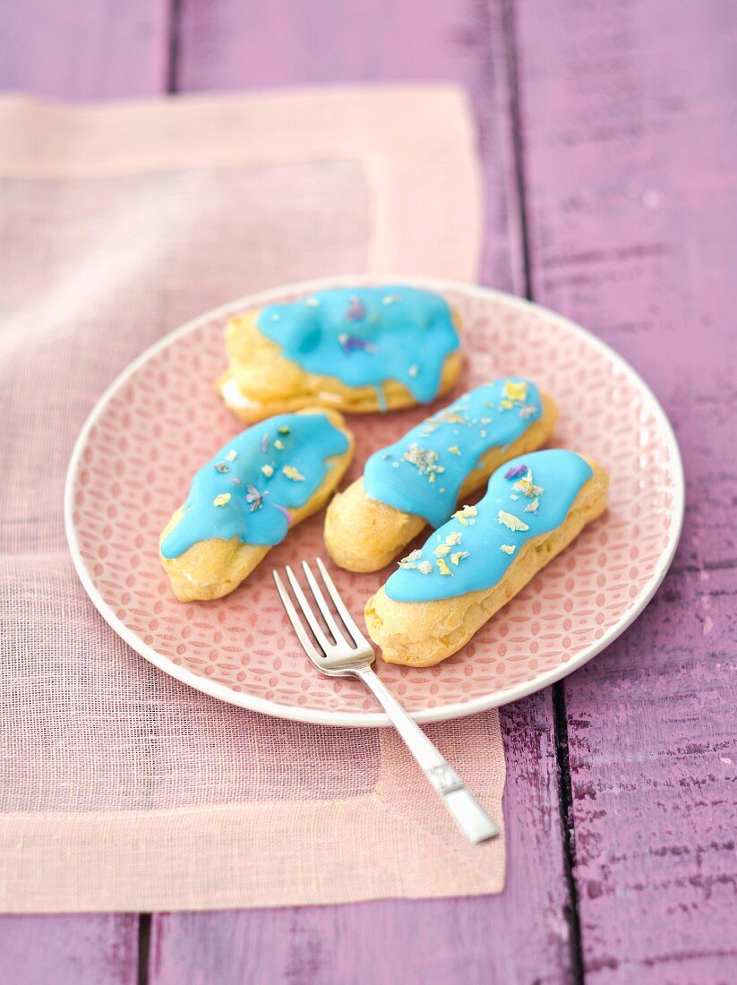 Eclairs with blue icing and dried pansy petals