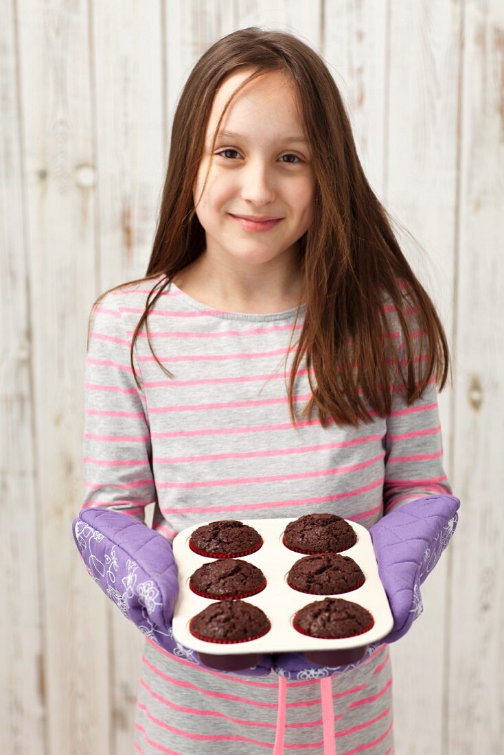 A girl holding freshly baked chocolate cupcakes