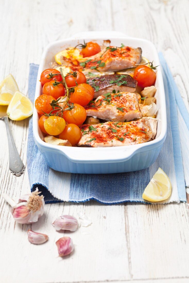 Baked salmon trout with potatoes, lemons and tomatoes