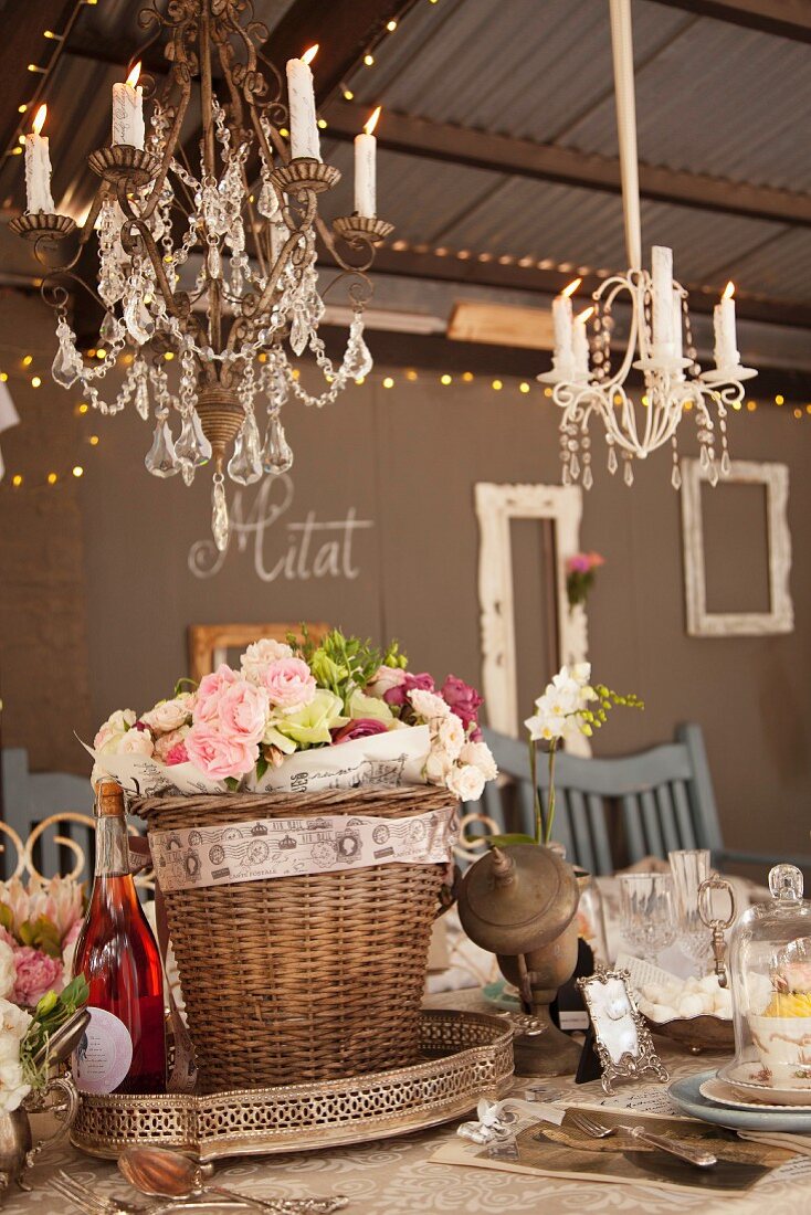 Geschmückter Korb mit Rosen auf festlich dekoriertem Tisch unter Kronleuchter mit brennenden Kerzen