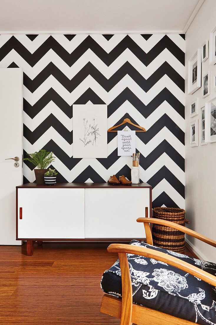 Sideboard with white sliding doors against wall covered in black and white geometric pattern