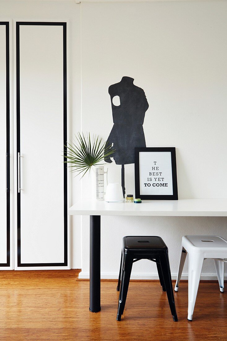 Black and white workspace with retro stools and table below silhouette of tailors' dummy painted on wall