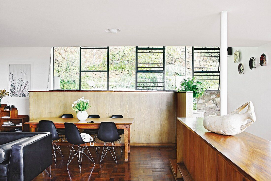 Black shell chairs in dining area in front of half-height partition and free-standing wooden sideboard in open-plan interior