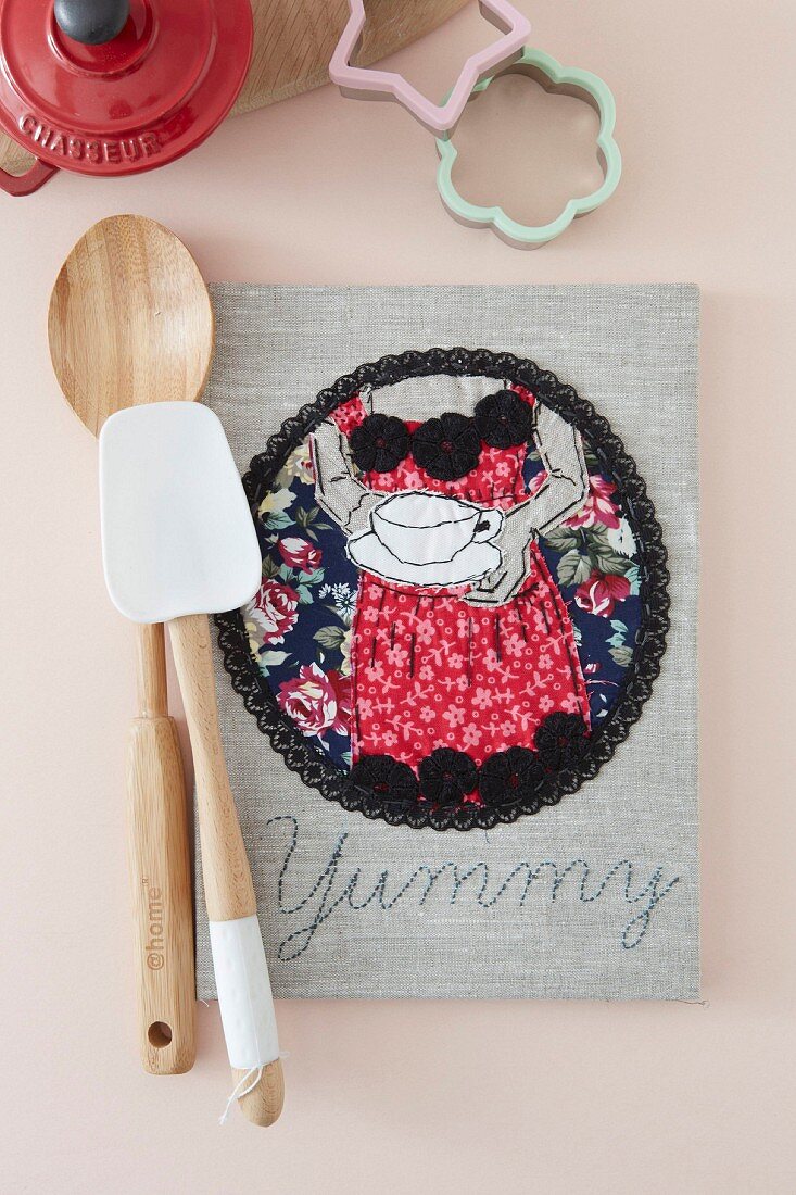 Hand-made cookery book with decorative motif on linen cover, wooden spoon and spatula