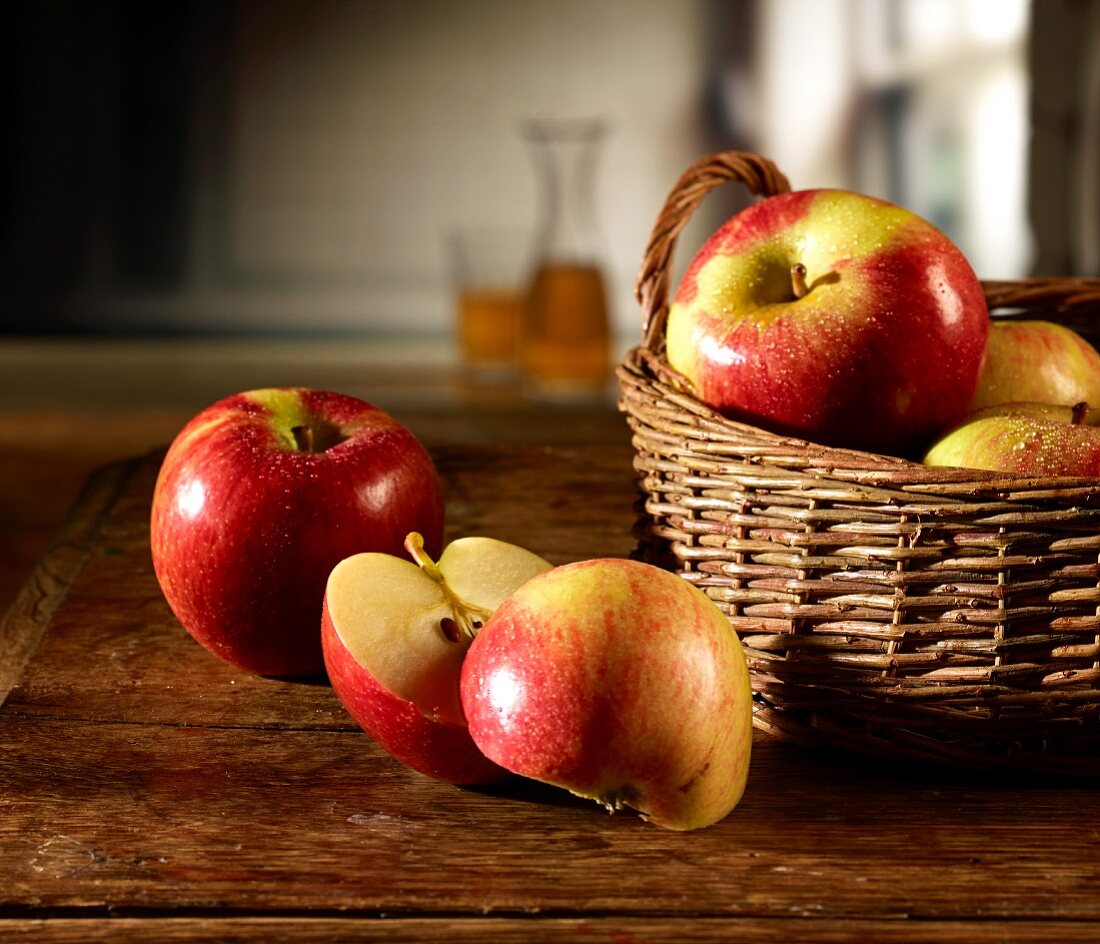 Red apples in a basket on a wooden table, one apple sliced