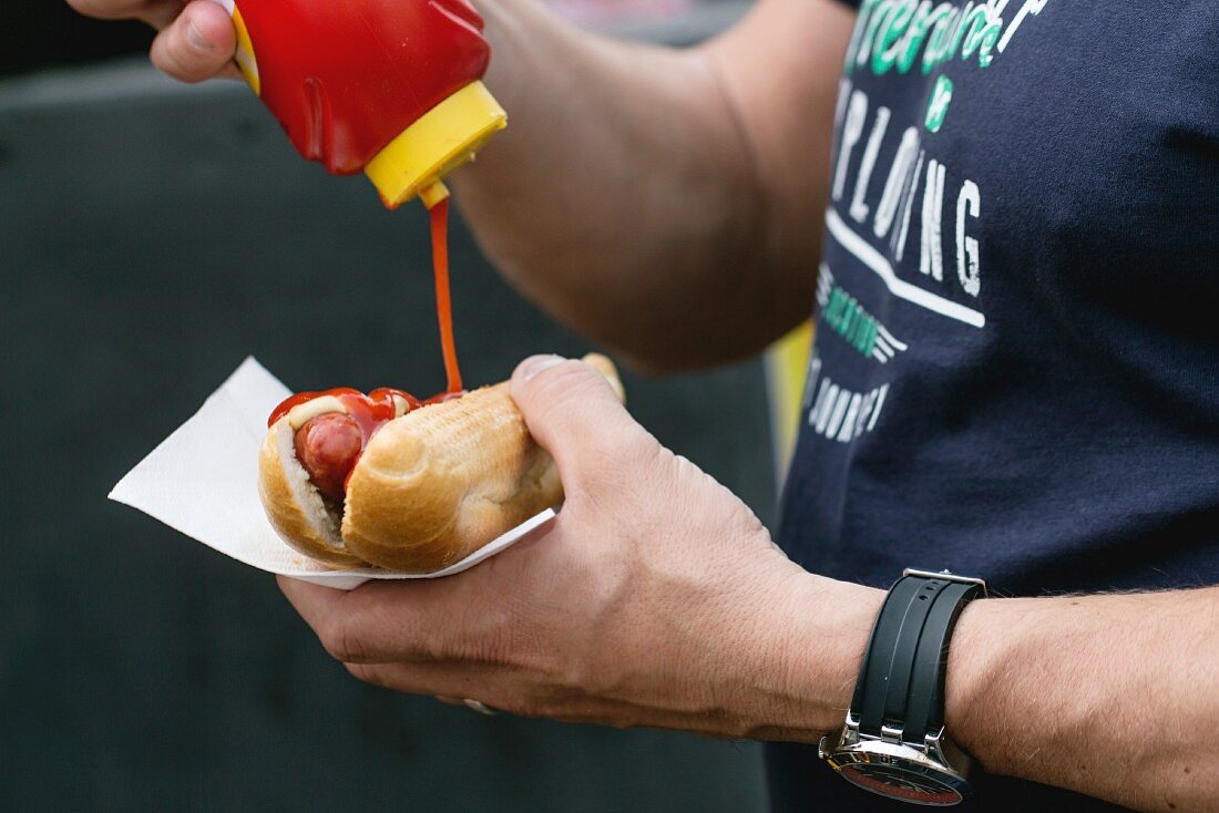 Mann giesst Ketchup auf Hot Dog