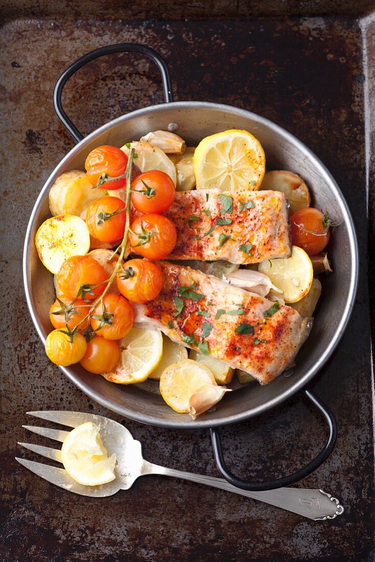Oven-baked salmon trout with potatoes, lemons and cherry tomatoes