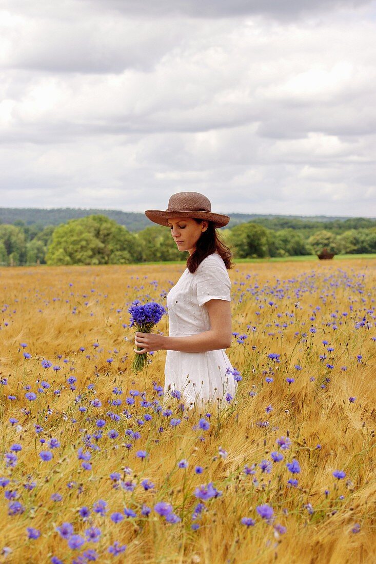 A woman in a corn field with a bunch of cornflowers