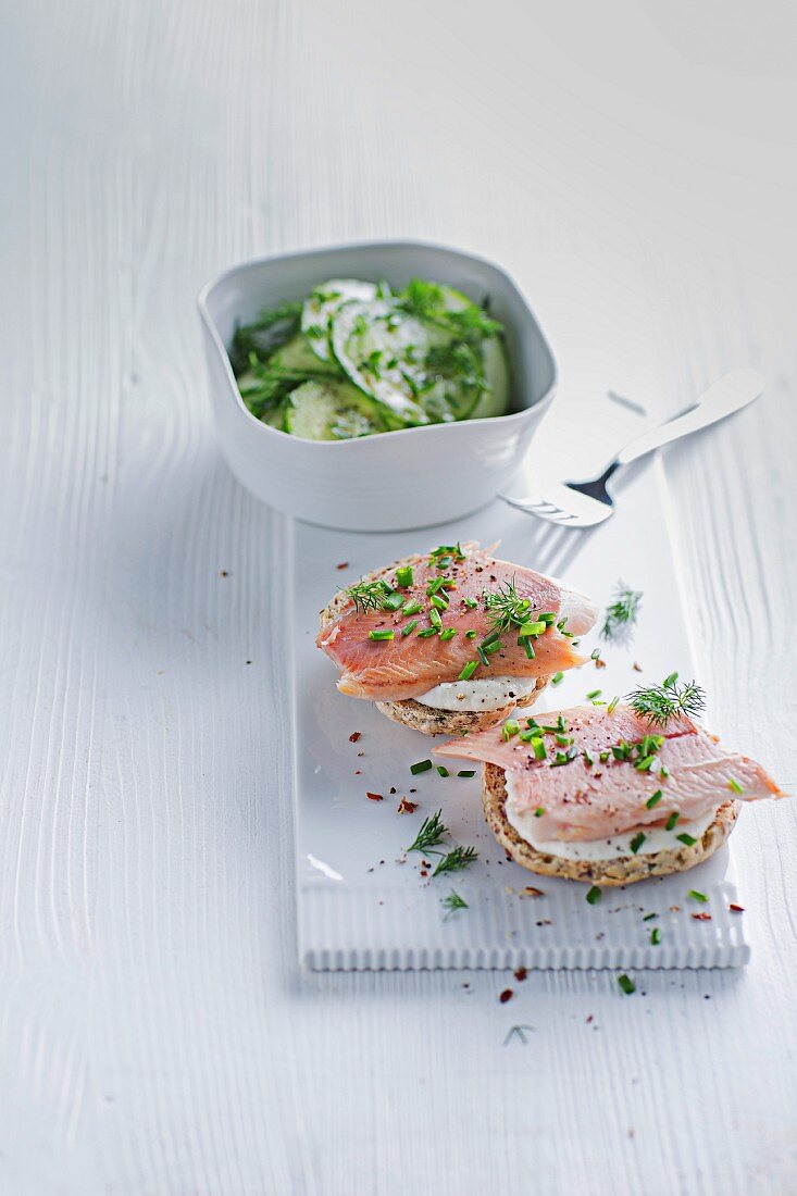 A herb bread roll topped with smoked trout served with a cucumber salad