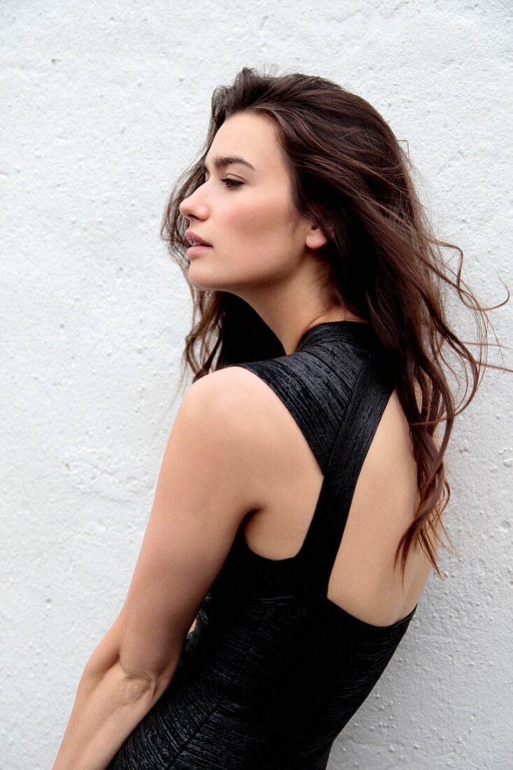 A young woman wearing a black dress standing against a white wall