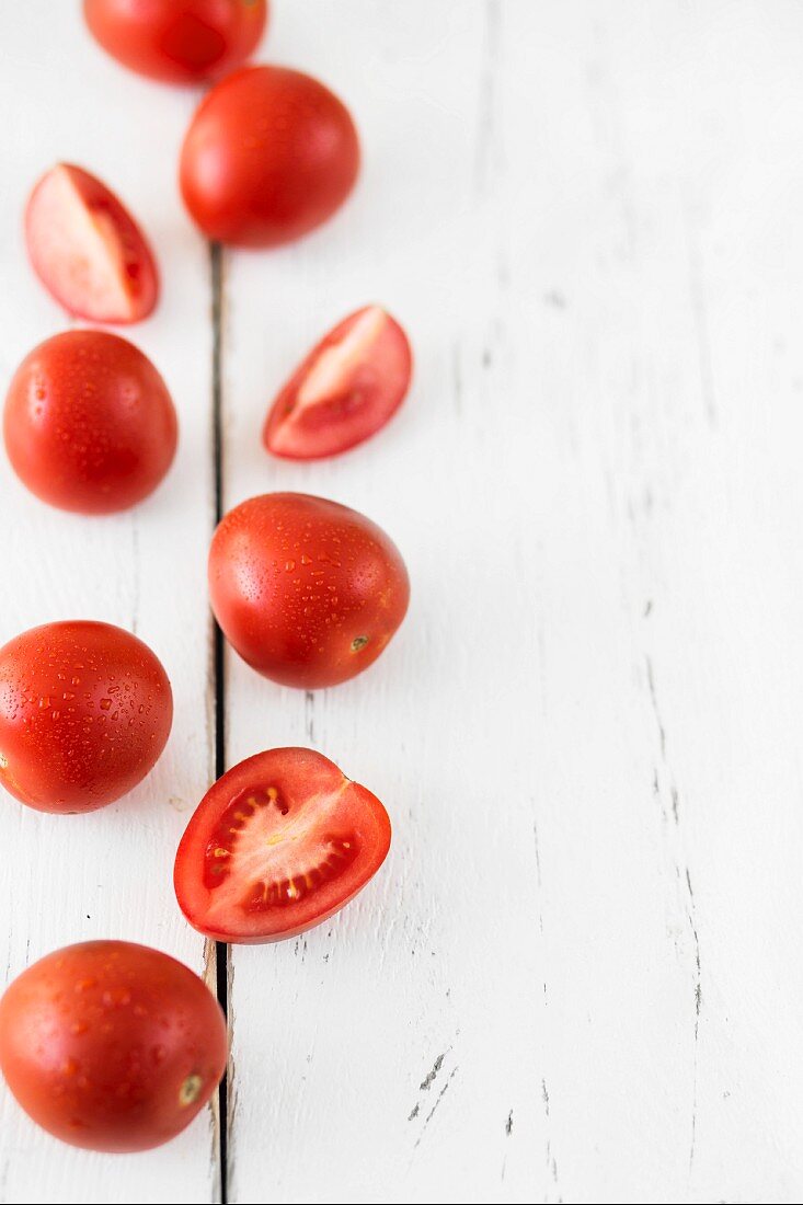 Tomaten und Tomatenhälften auf weißem Holzuntergrund