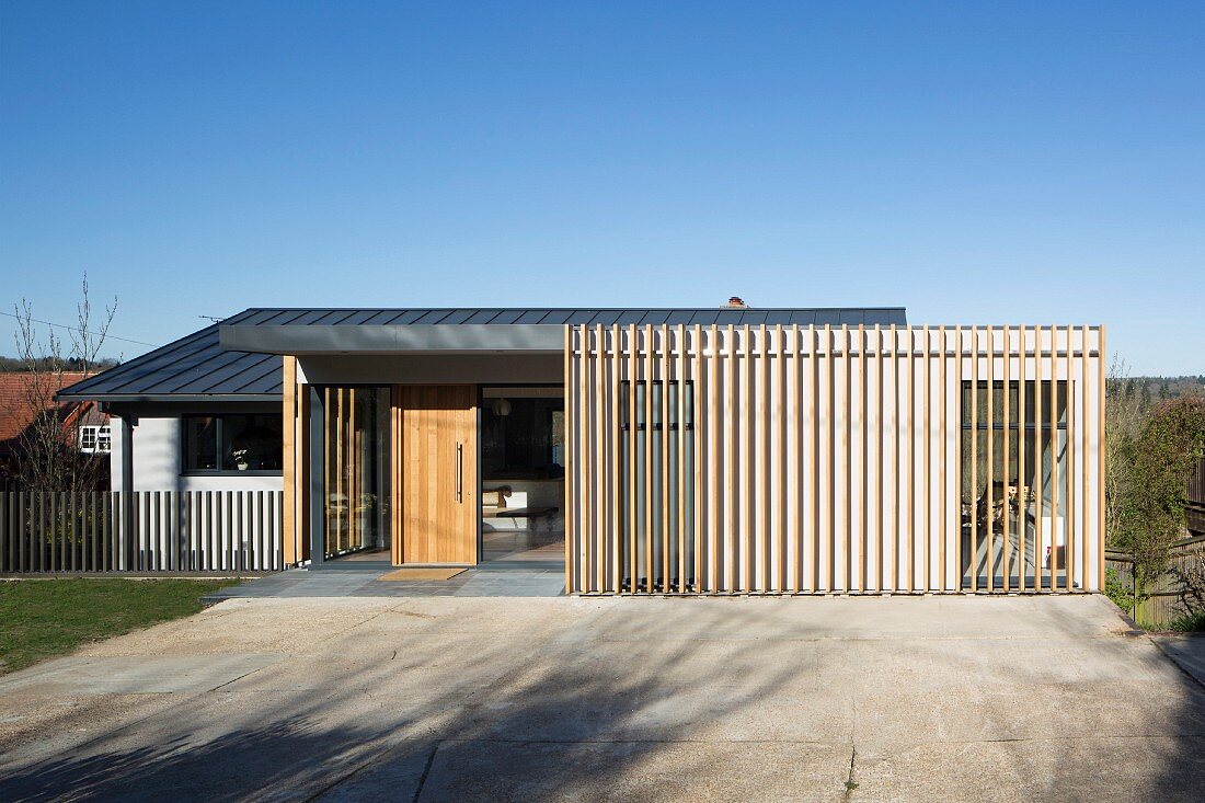 Blue sky above contemporary house; wooden front door, glass walls and wooden structure in front of facade