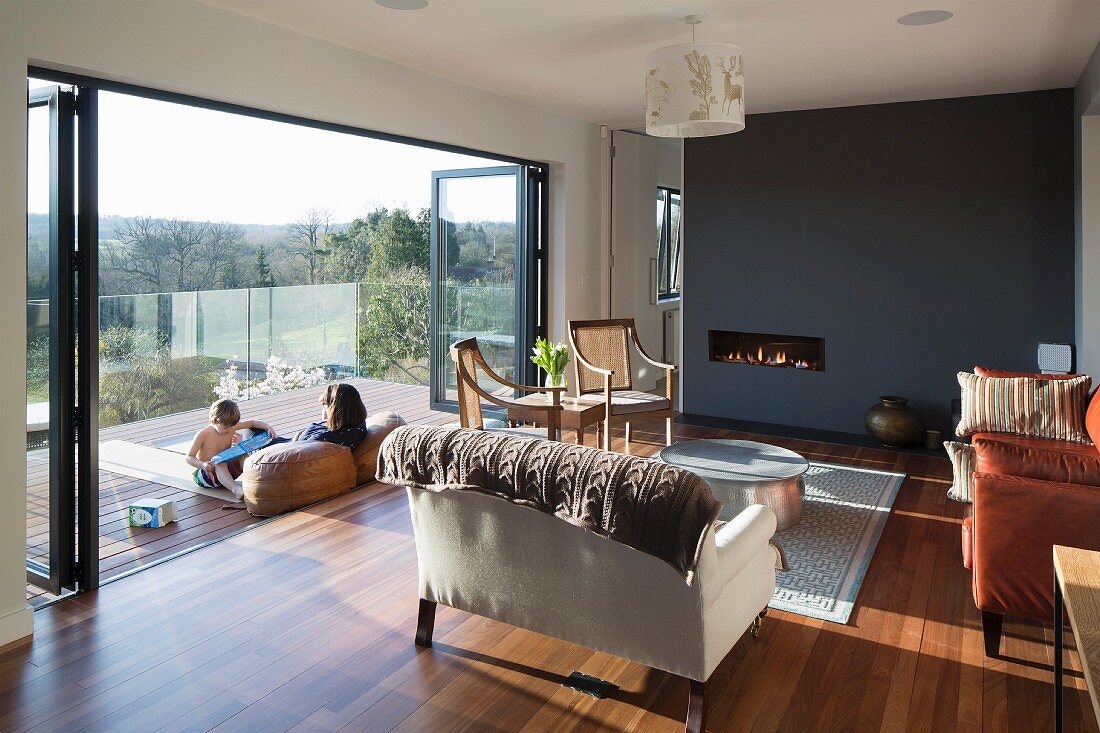 Eleganter traditioneller Wohnraum mit Ledersofa und antiken Stühlen, im Hintergrund dunkelgraue Wand, Familie in warmer Frühlingssonne auf dem Balkon mit Landschaftsblick