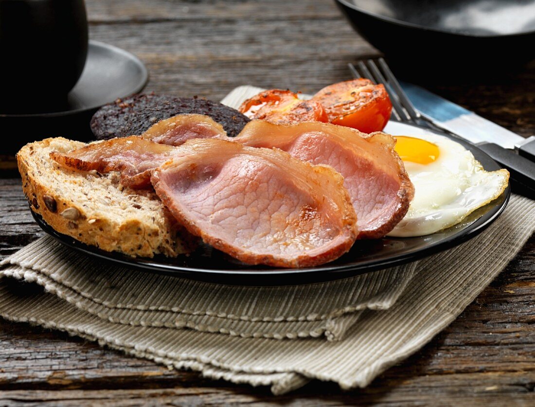 An English breakfast with bacon, fried eggs, tomatoes and black pudding