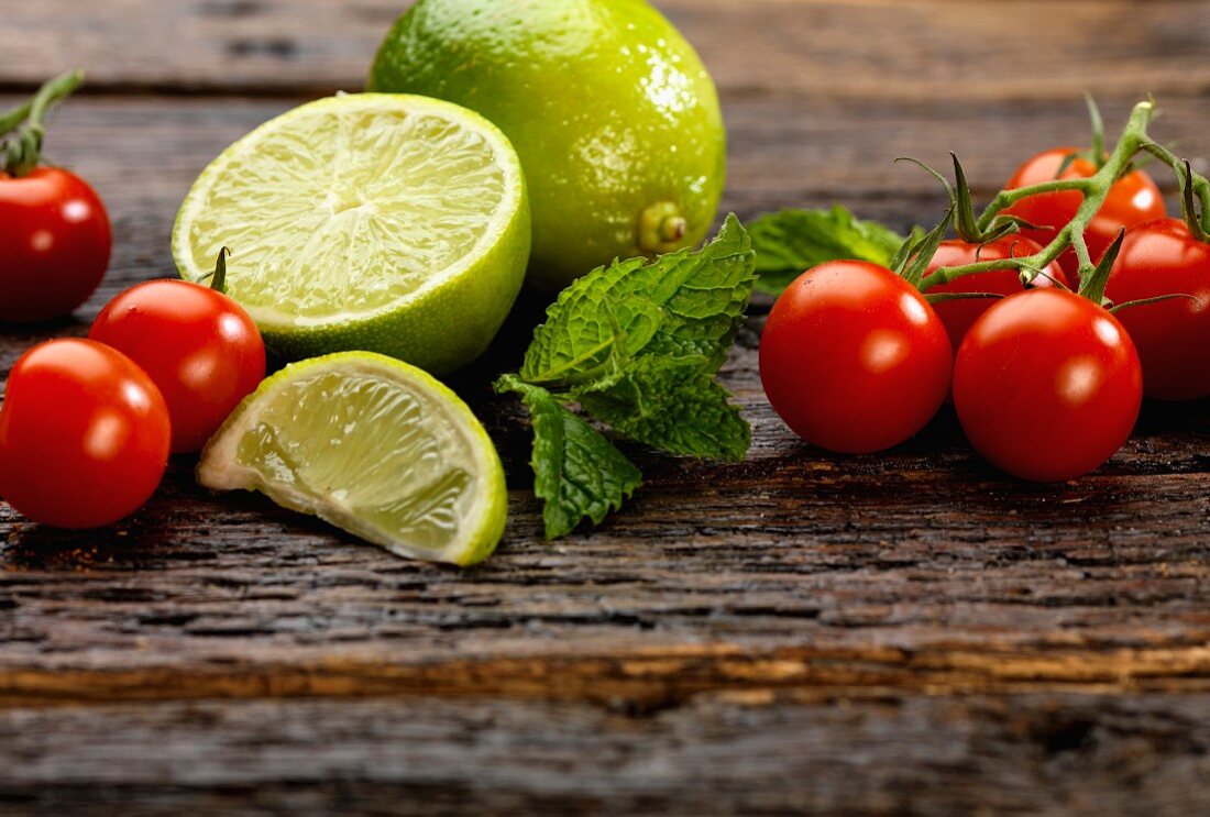 Cherry tomatoes, mint and limes on a wooden surface