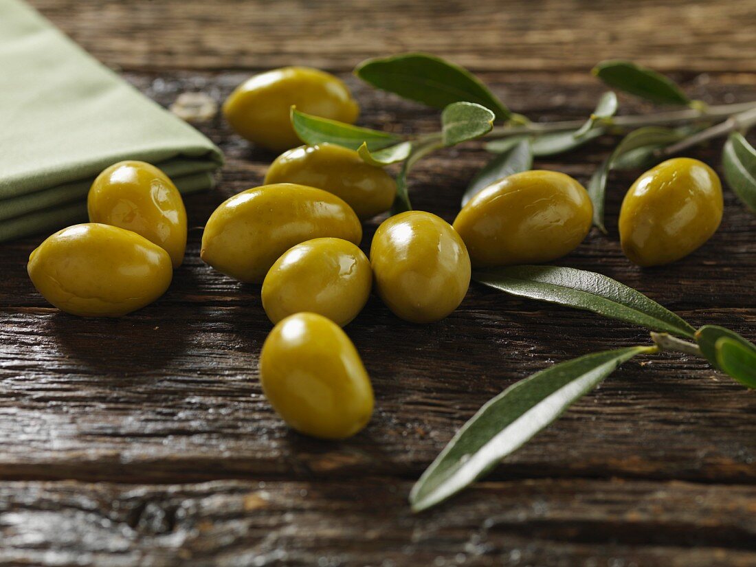 Green olives with leaves on a wooden surface