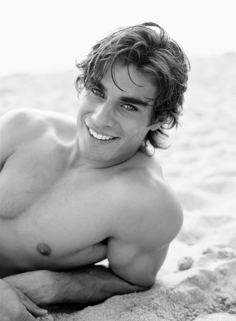 A young, topless, smiling man lying on a beach (black-and-white shot)