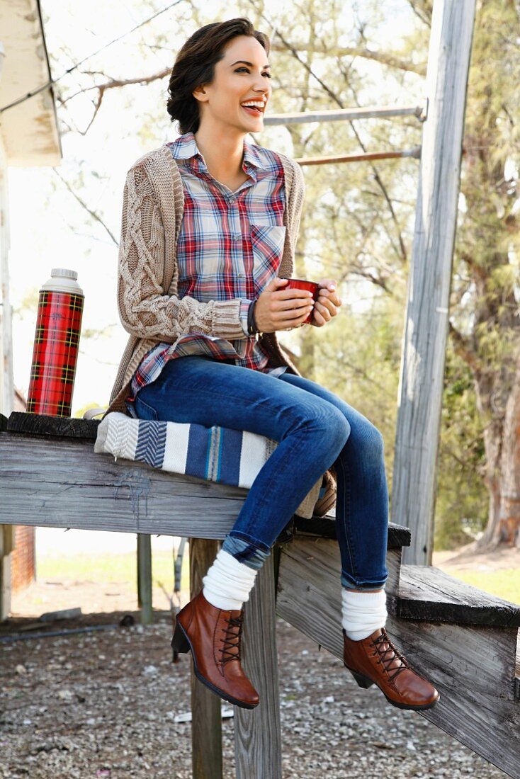 Frau in Karohemd, Jeans und Strickjacke sitzt auf Holztribüne