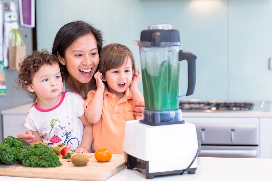 A woman mixing a smoothie for little girls in a kitchen
