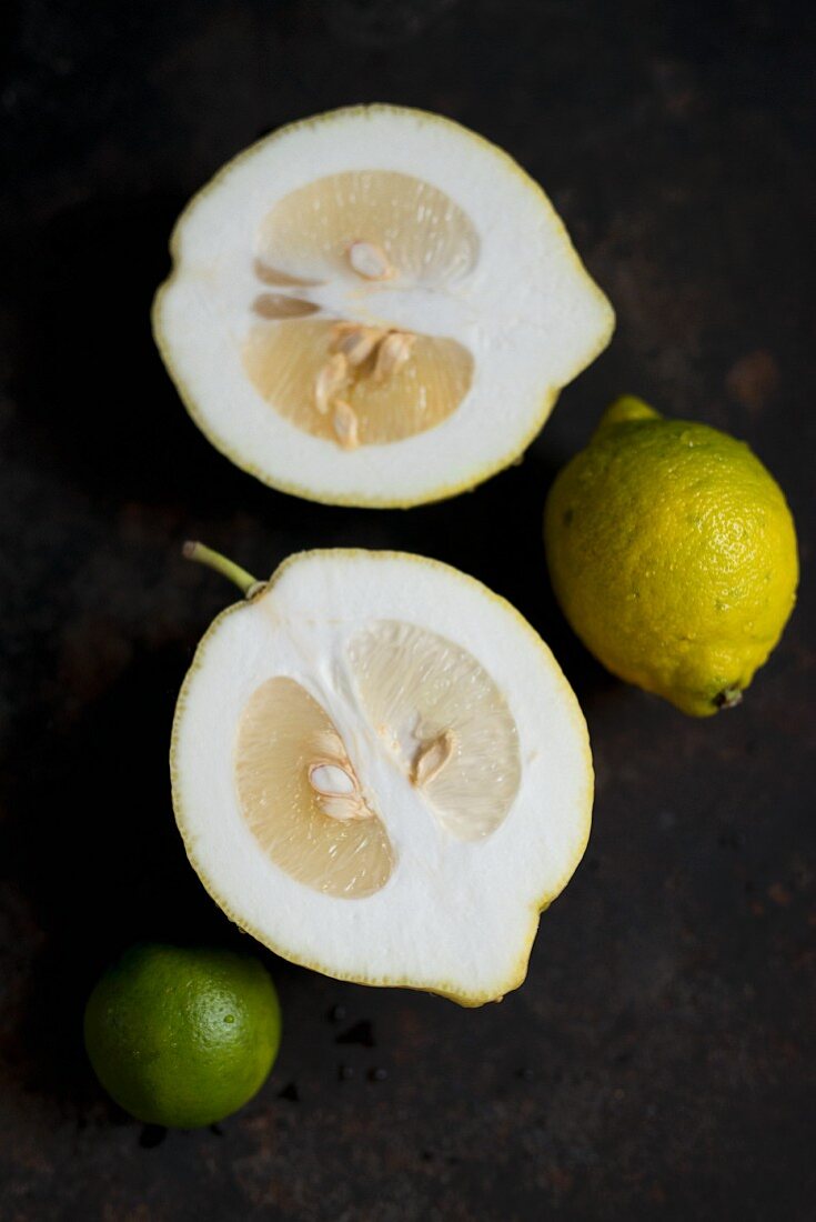 A halved citron next to a lemon and a lime