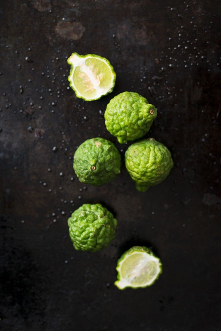 Kaffir limes, whole and halved on a black background (seen from above)