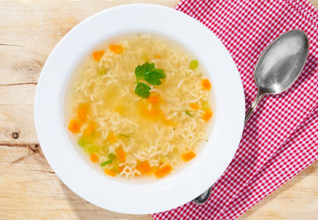 Buchstabensuppe im Teller mit Löffel auf Holzuntergrund