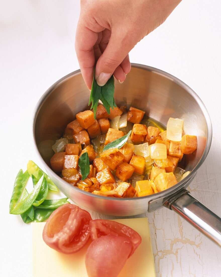 Süßkartoffelcurry, Blätter vom Bockshornklee zu angebratenen Kartoffelwürfeln geben